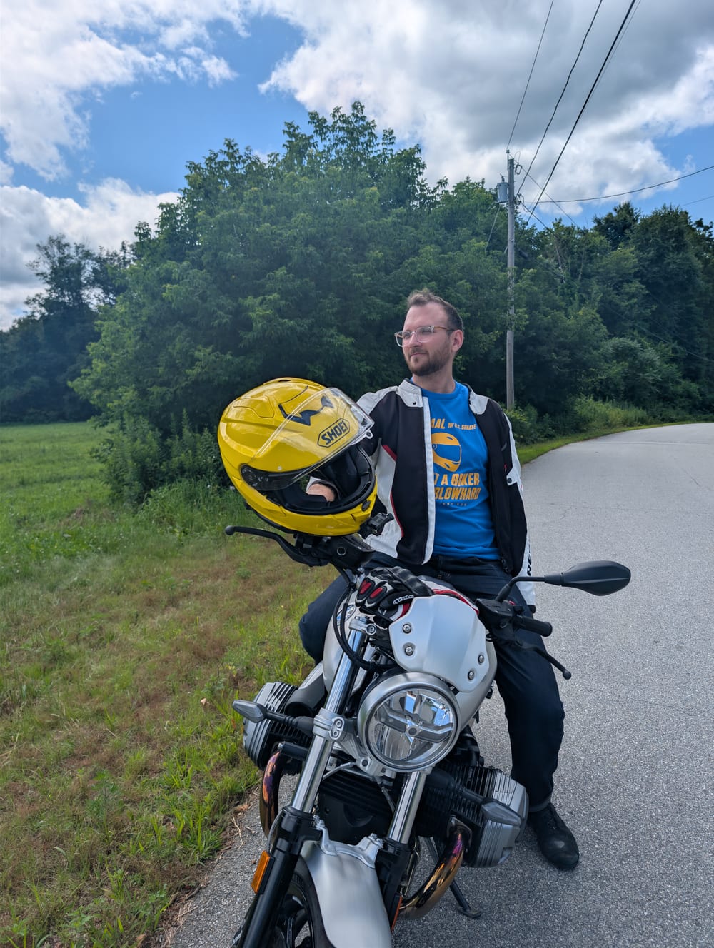 Max Saal on his motorcycle on a New Hampshire back road, yellow helmet in hand